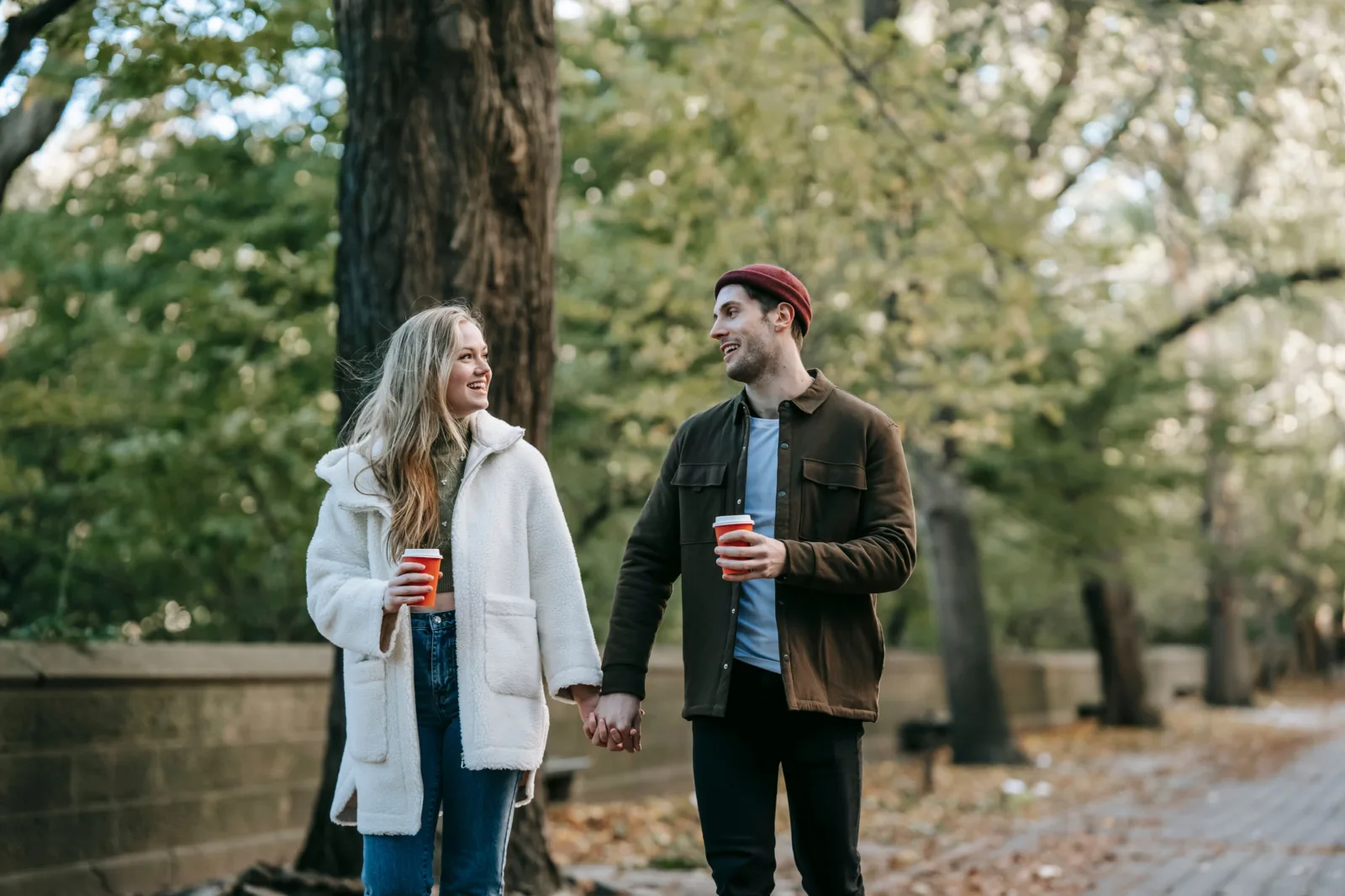A couple enjoys a romantic walk in the park during autumn, sipping coffee and holding hands